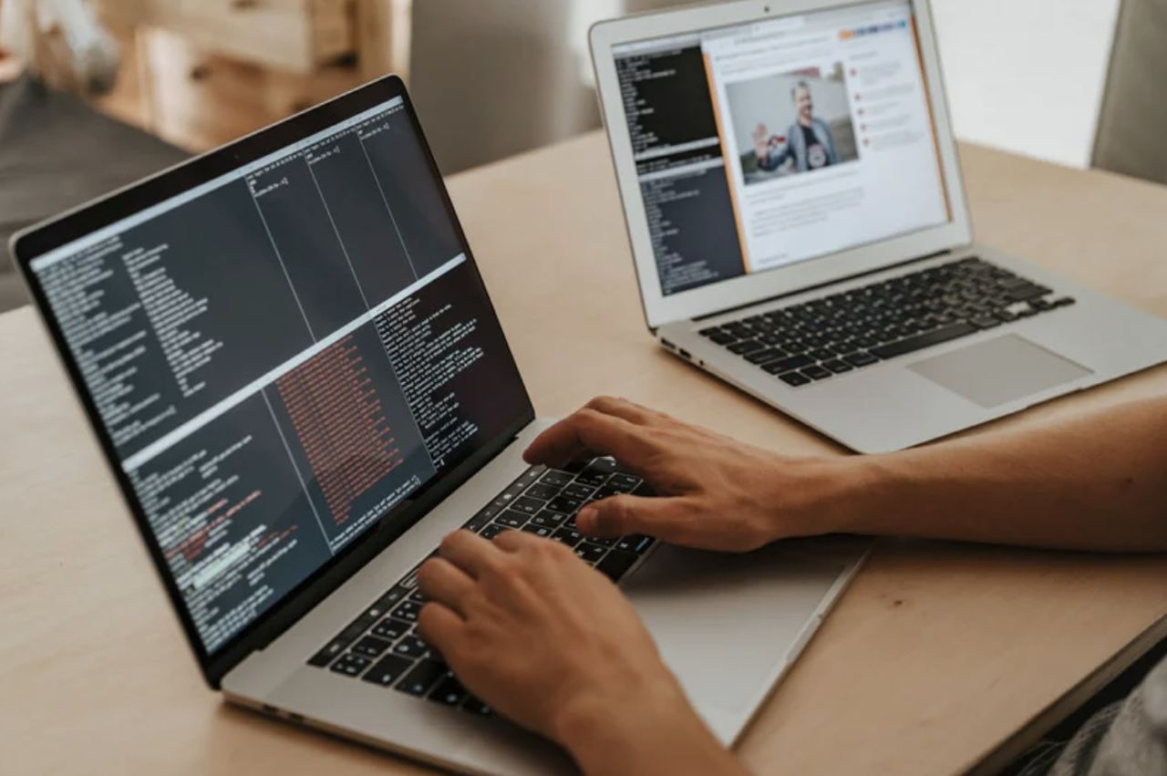 a man working with two MacBooks and writing codes