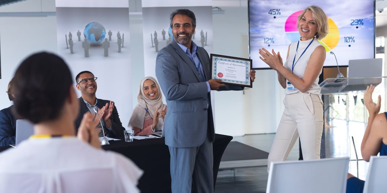 a woman employer rewarding a male employee and people applauding them