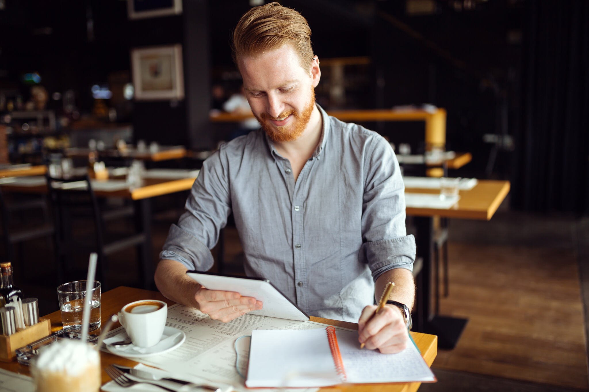 Businessman taking notes at a coffee with a cup of coffee at the table looking at his notes