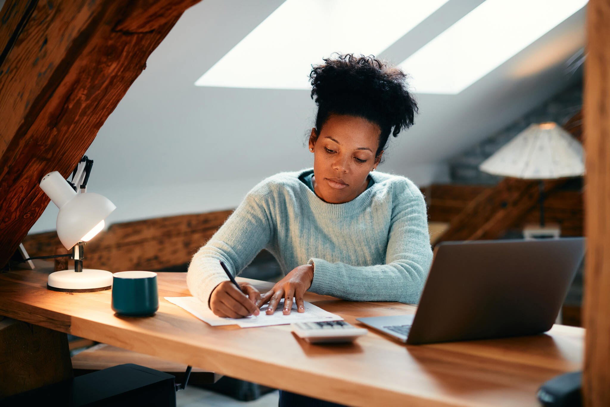 African American woman taking notes while working at the table with her laptop