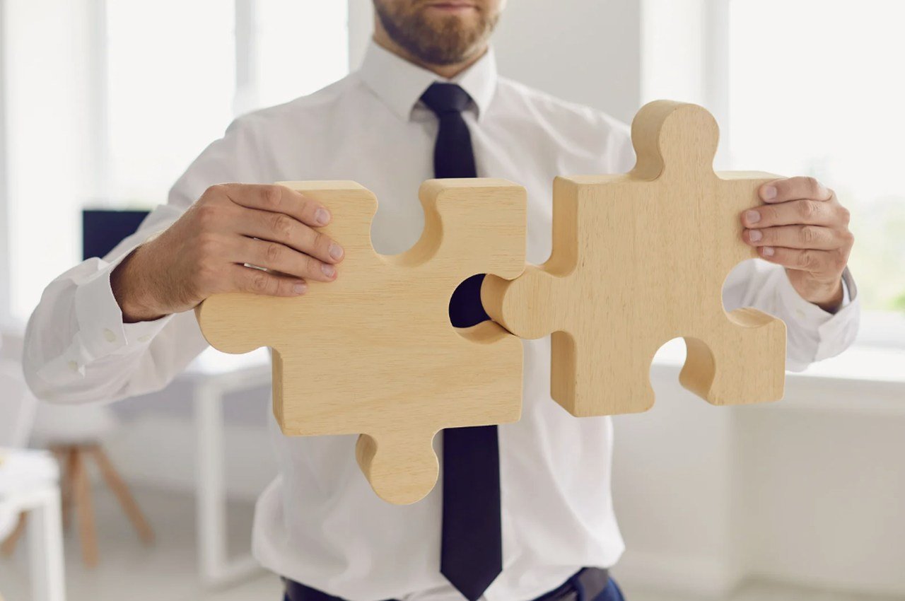 a picture of a man in white dress and a black tie holding two pieces of wooden puzzle showing how software integration connects two disjoint parts