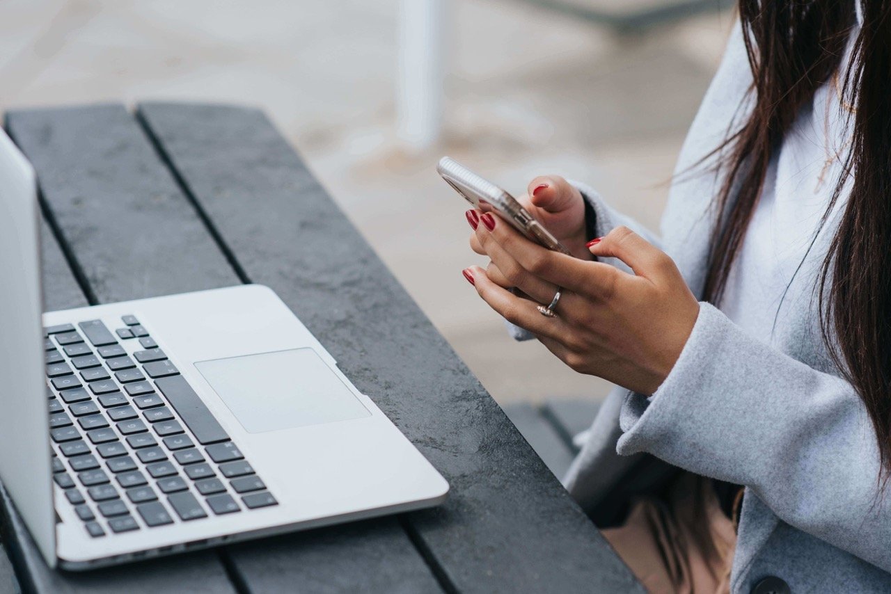 woman checking smartphone near laptop on table