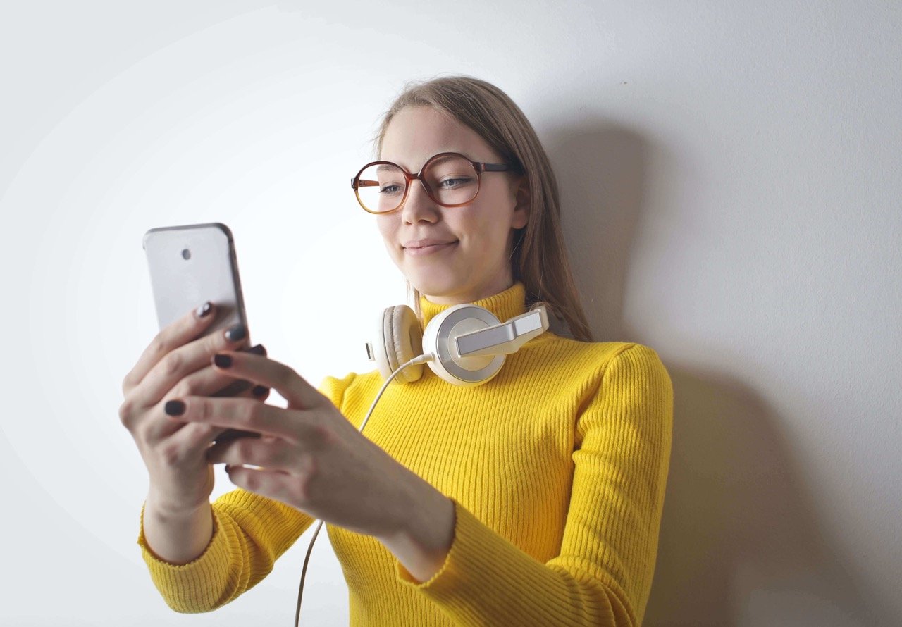 woman in a yellow turtleneck sweater with headphones checking her phone