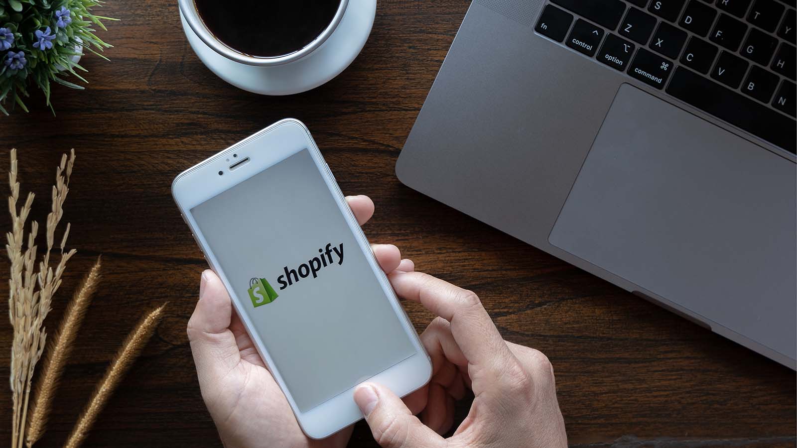 an stock image of a hand holding a phone that is showing the Shopify logo