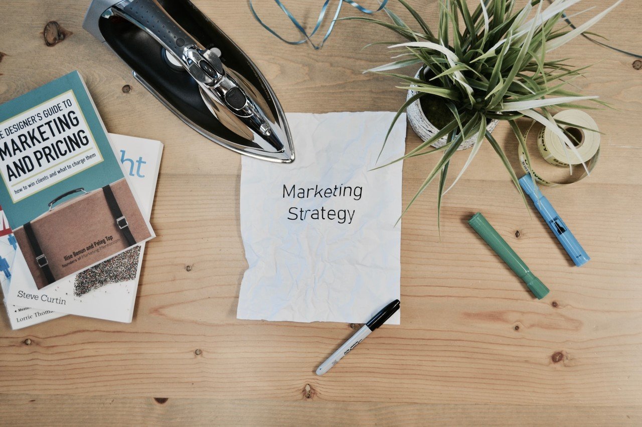 "marketing strategy" written on a paper next to books, flowers, pencils and iron