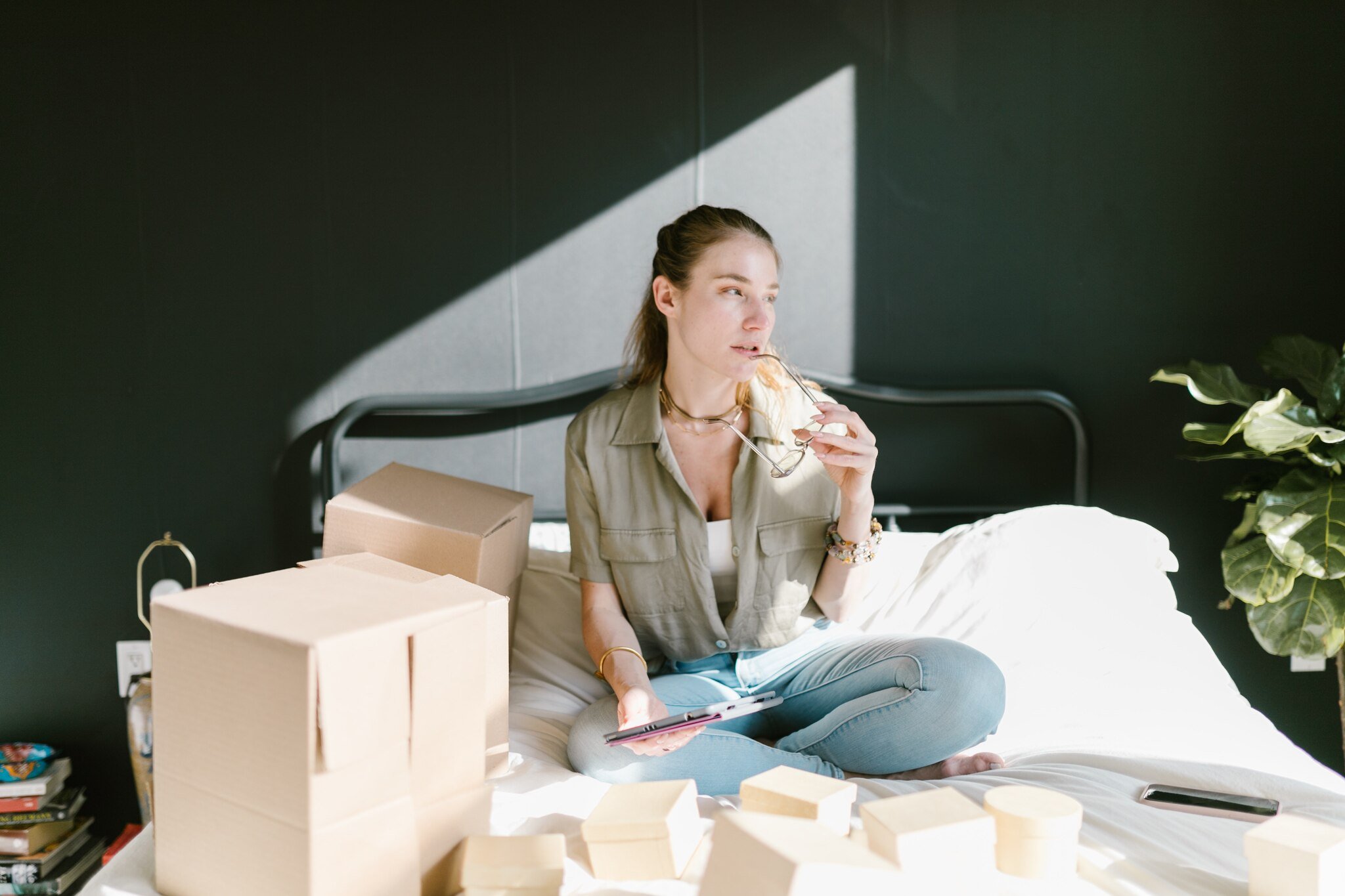 a woman preparing cardboard boxes on a bed and holding a glasses