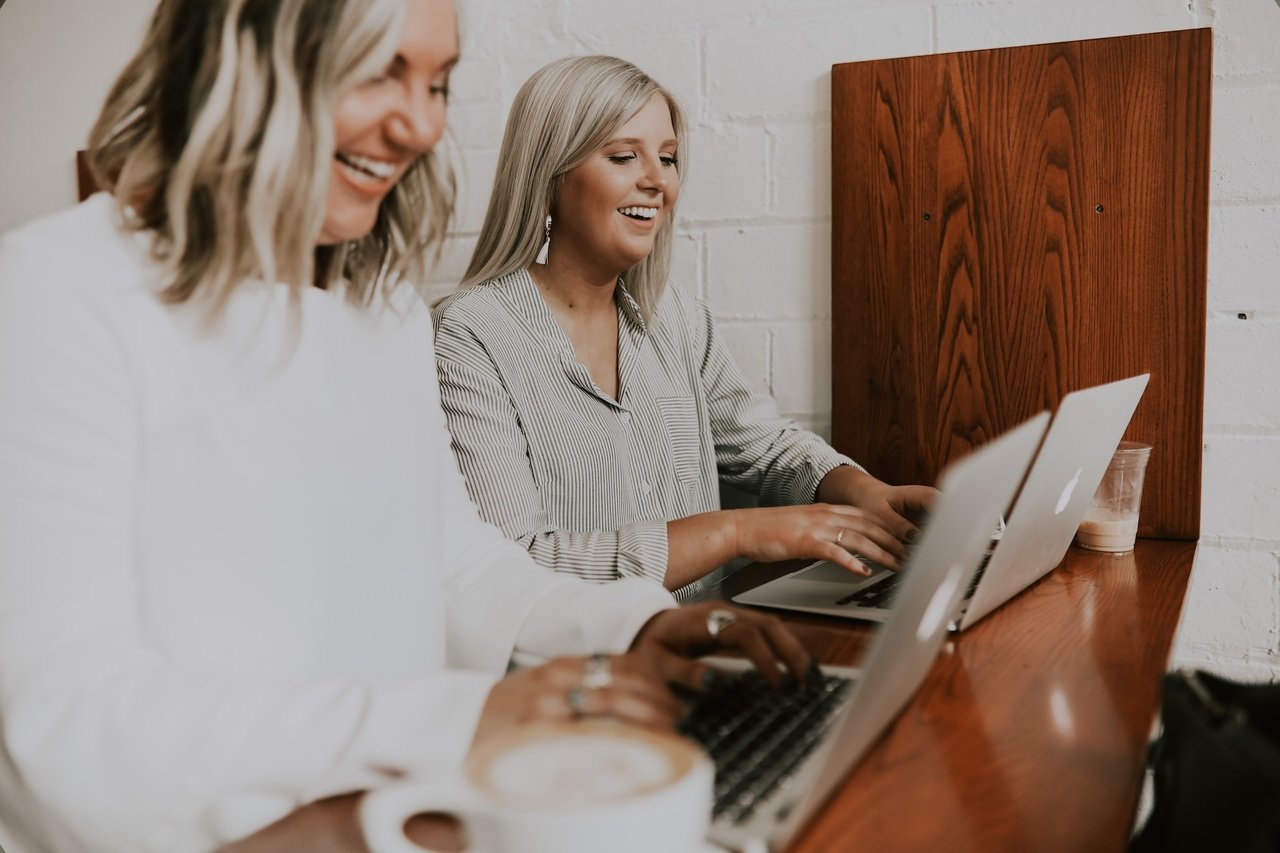 two women working with their laptops and laughing