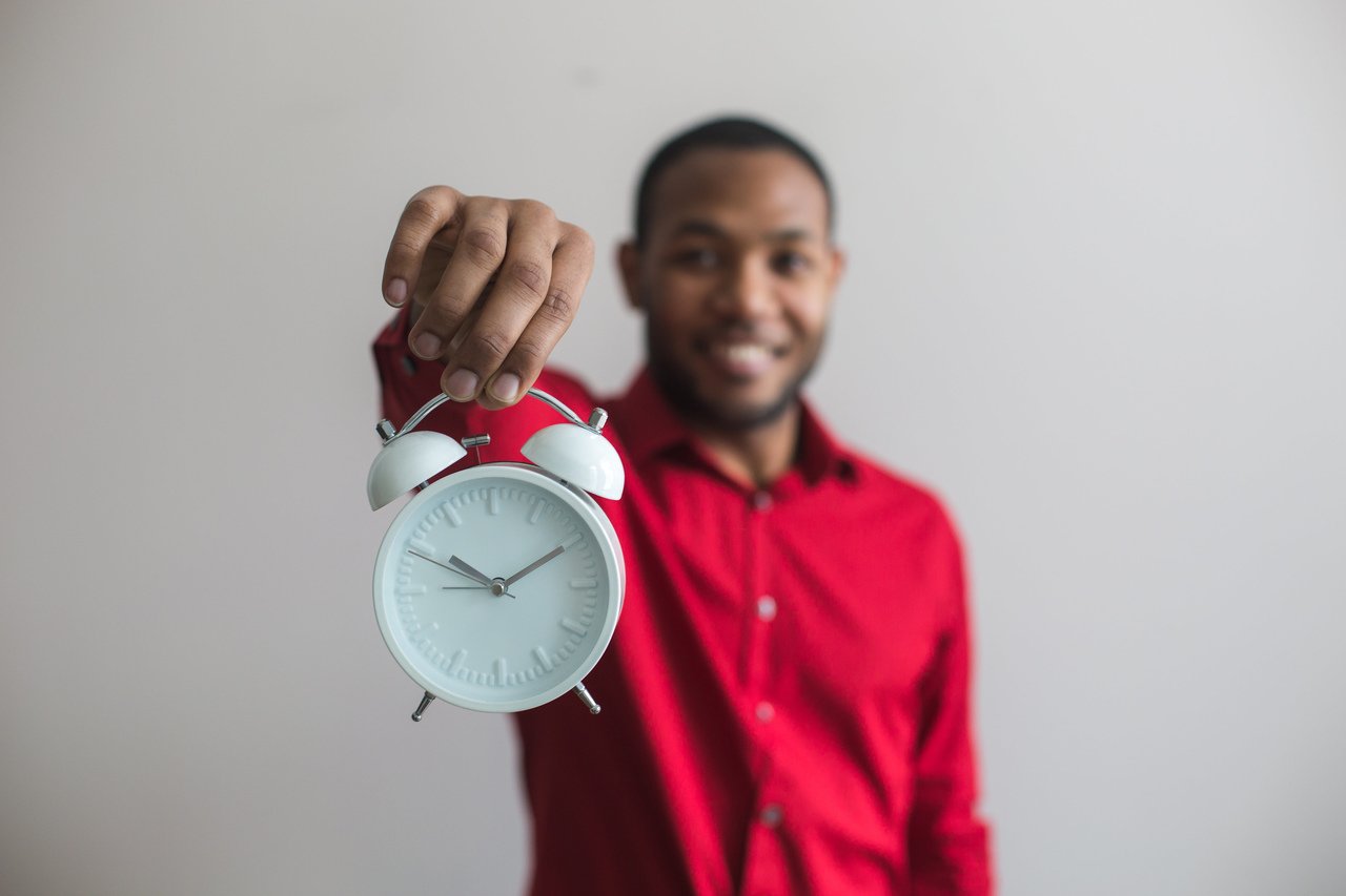 a man wearing red sweater smiling and holding clock forward