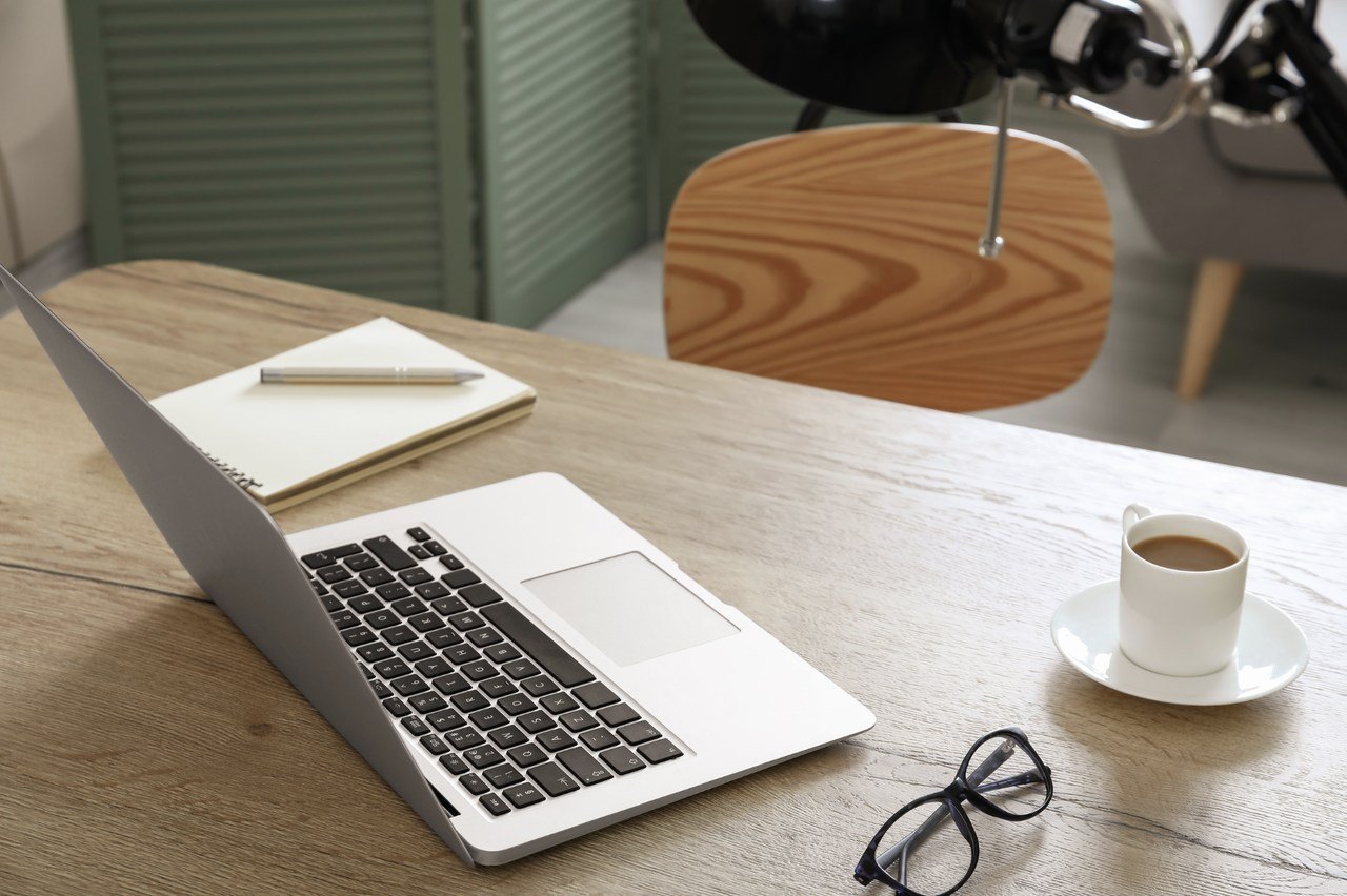 a wooden working table with laptop on top of it next to a coffee mug and a notepad