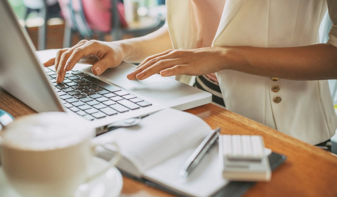 hands typing on a laptop with a coffee mug and books on the table around it