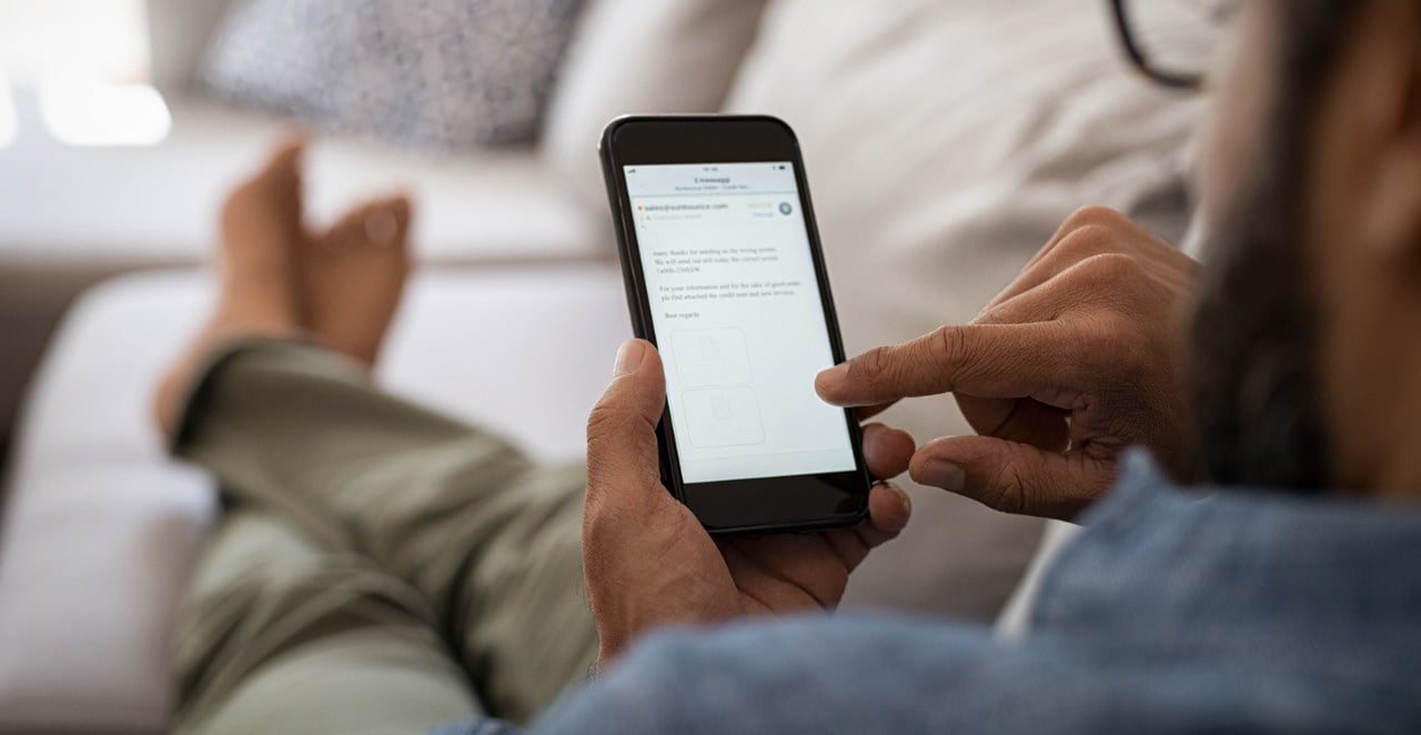 a person checking his emails on a smartphone while laying on a couch; only the hands holding the phone, legs and feet of the person is visible