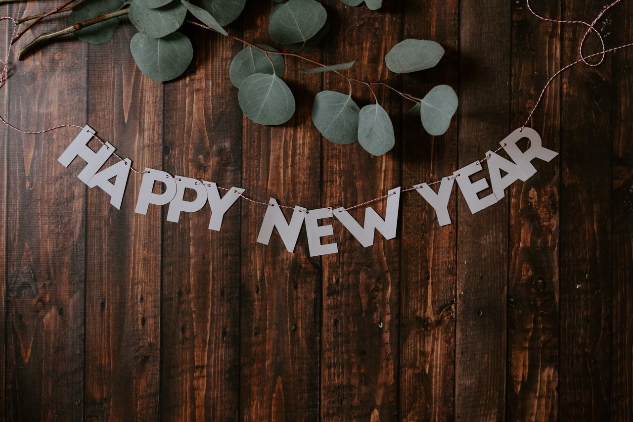 a decoration that says "Happy New Year" with leaves on the wooden ground