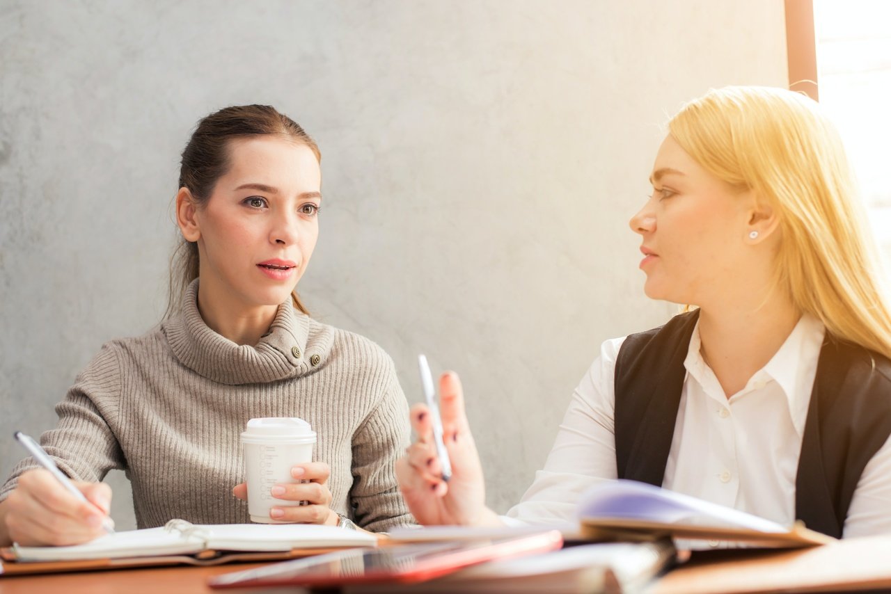 two women holding pen and speaking