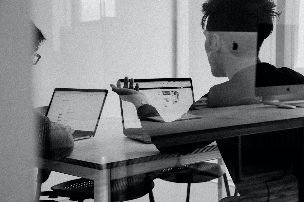 two people working and using laptops while talking with each other