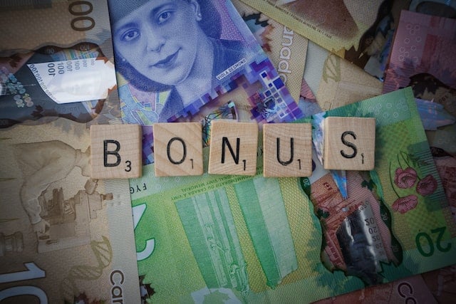 The scrabble letters of "bonus" side by side on a background consisting of different kinds of paper money