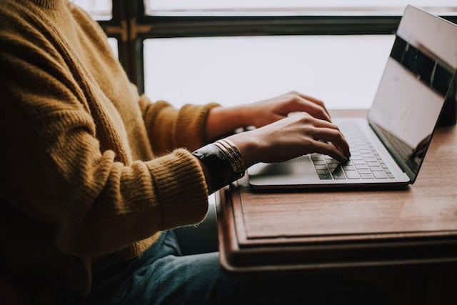 Hands of a person on laptop, sitting at the table next to a window