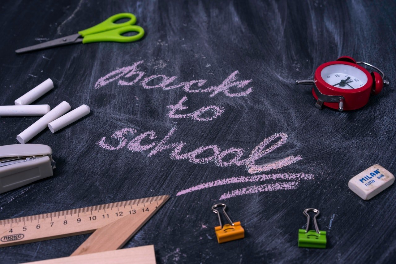 an image of "back to school" written on a blackboard along with school supplies like a scissor, a chalk and a clock