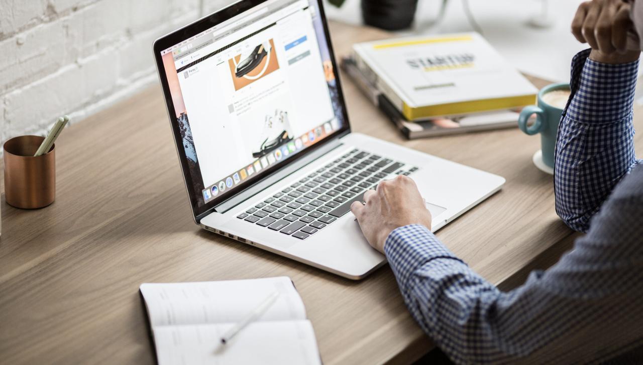 hands working with a laptop that is placed on a working desk next to other books and an open notebook