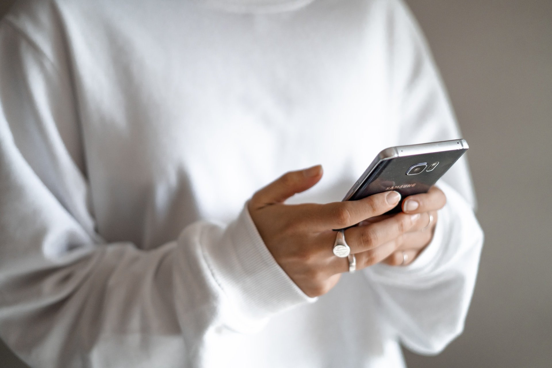 a woman holding a phone and wearing a white jumper