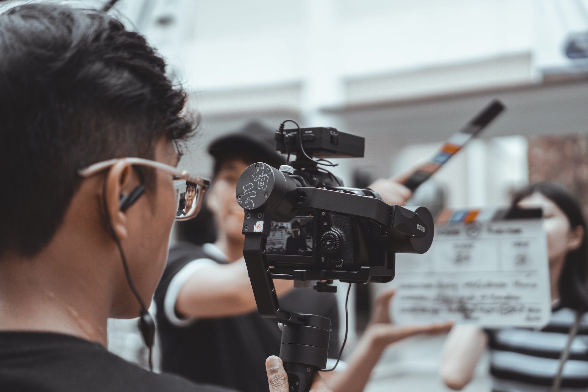 a man wearing glasses holding a camera and shooting a video