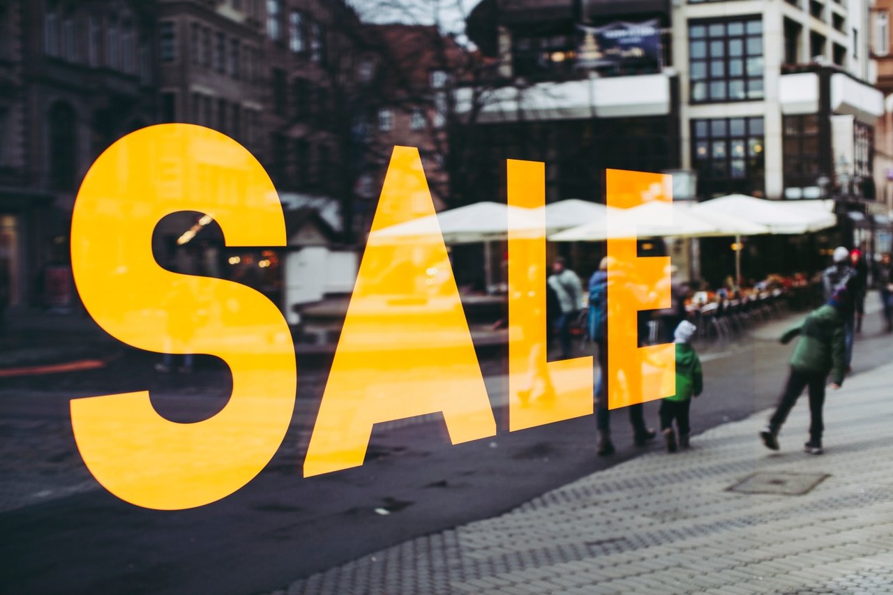 Yellow "Sale" sign on a store window reflecting people and street