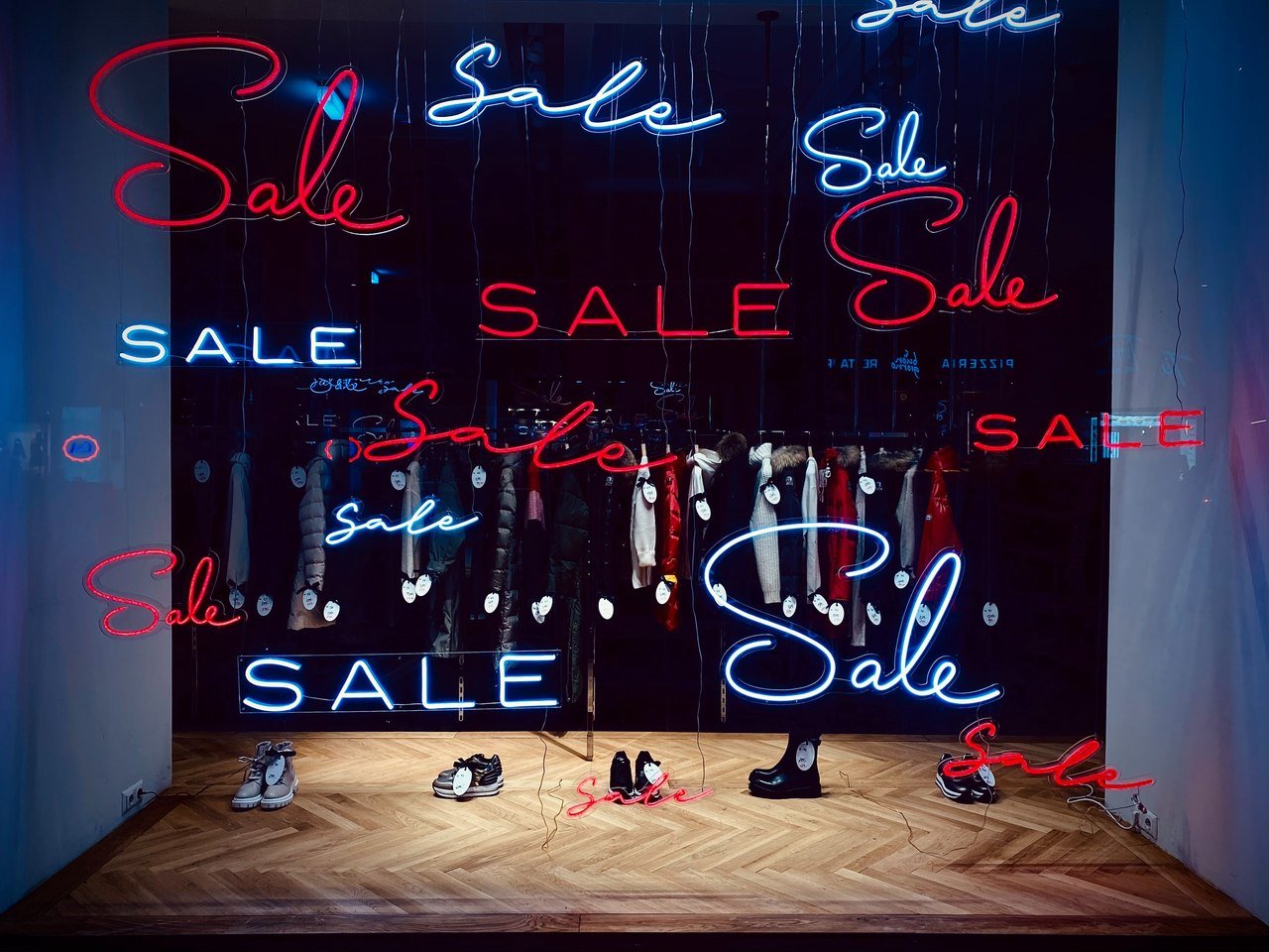 Different style "Sale" written in neon red and white on a store window showcasing shoes