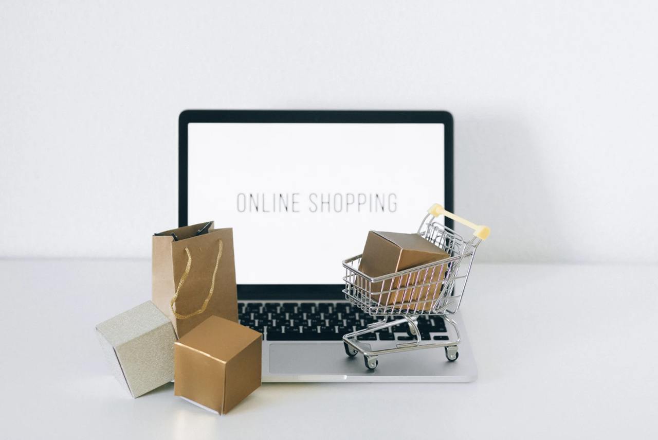 an image of a macbook that shows a white screen that says "Online Shopping" with some little shopping carts and bags in front of it on a desk