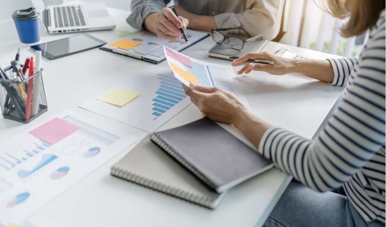 two hands is showing in the picture one is holding papers and the other one a pen, while working on a desk