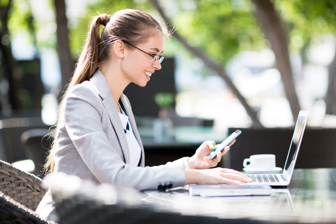 a woman working outdoor and smiling at her computer