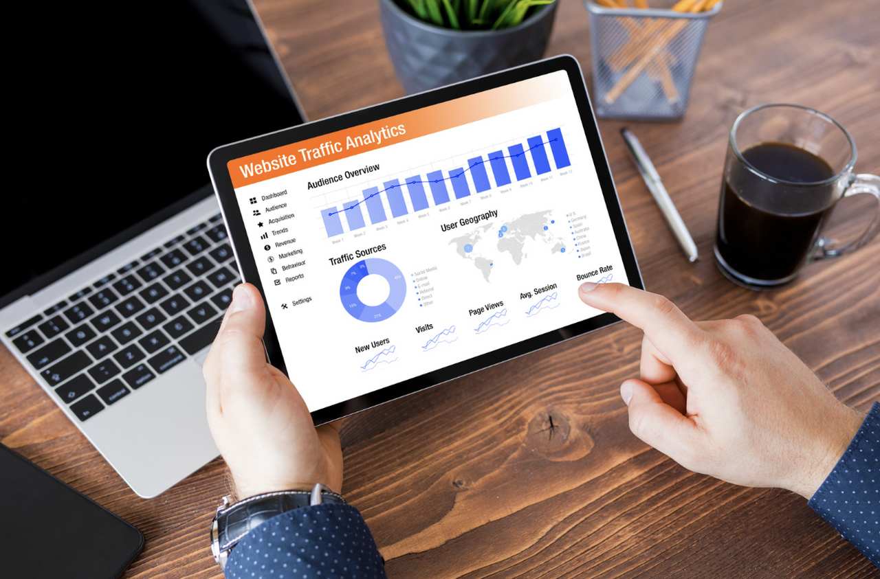 an image of a man's hands working with Google Analytics tool on a tablet with a glass of coffe on the desk