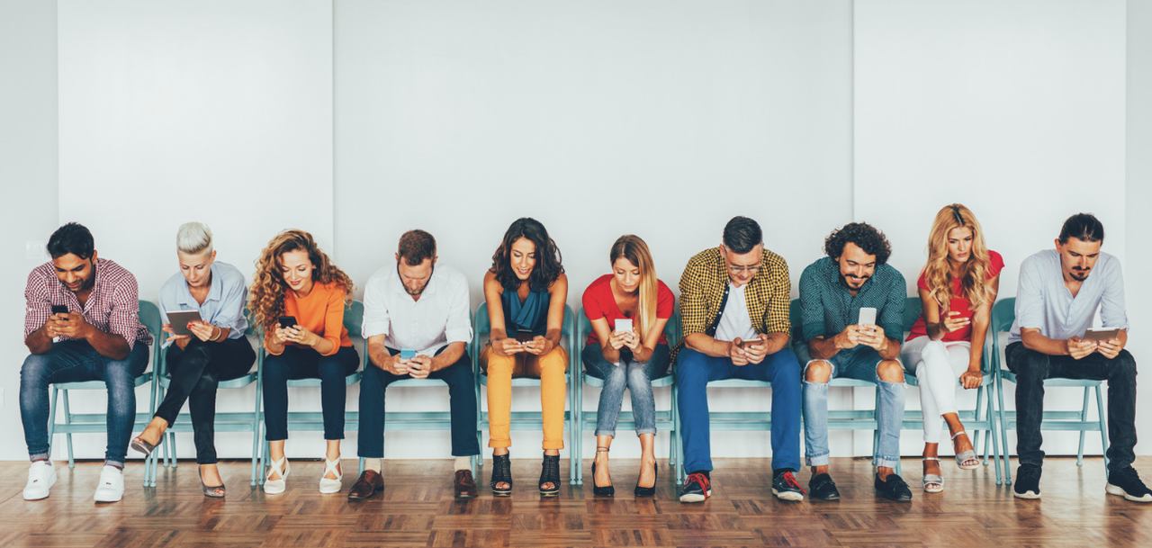 Poeple working with their smartphones sitting on a bench next to each other