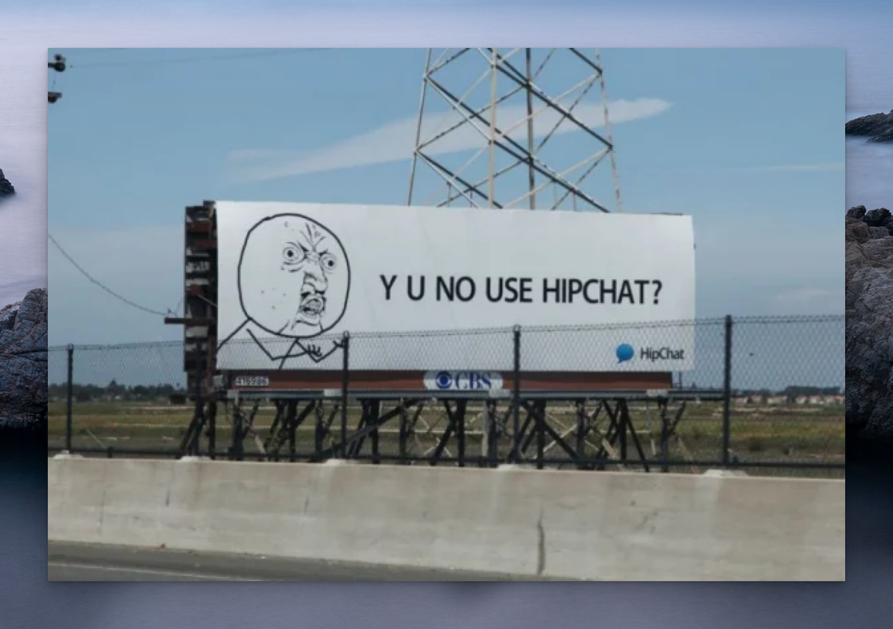 HipChat's billboard advertisement with a with an angry cartoon figure with the text "Y U NO USE HIPCHAT?" next to it on a billboard; the billboard is visible behind a fenced wall 