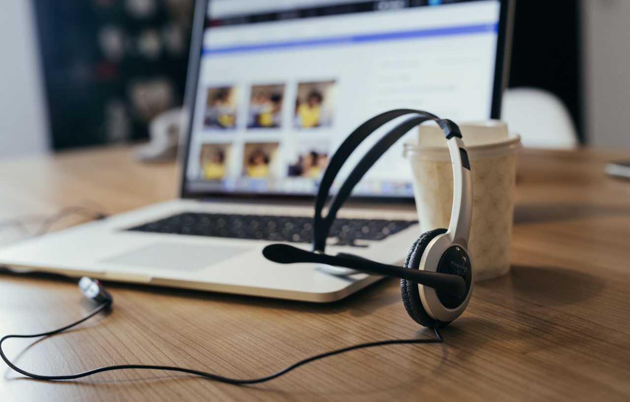 a picture of a customer support desk with a headsets, laptop and a cup of coffee