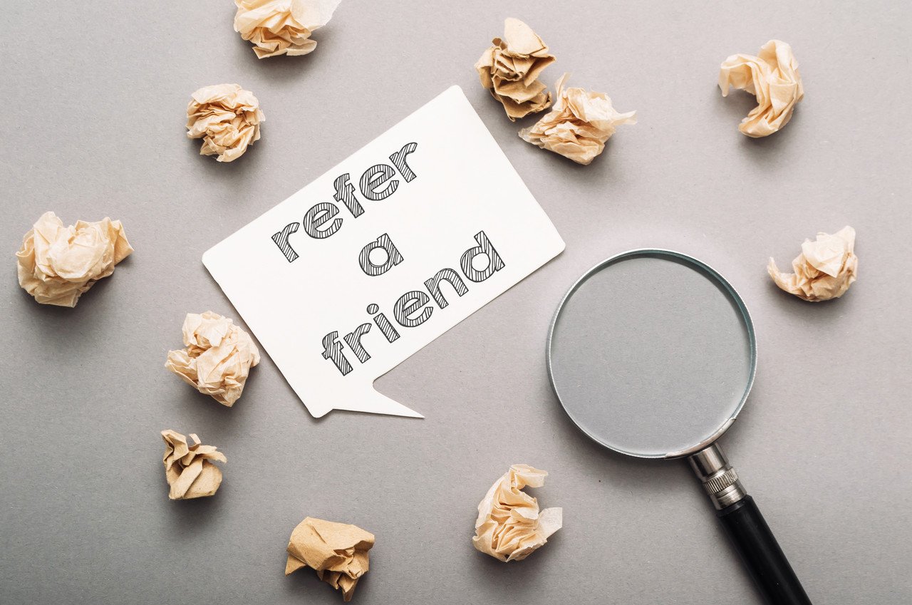 text refer a friend on a white speech bubble on a gray background with a magnifying glass and paper pieces around