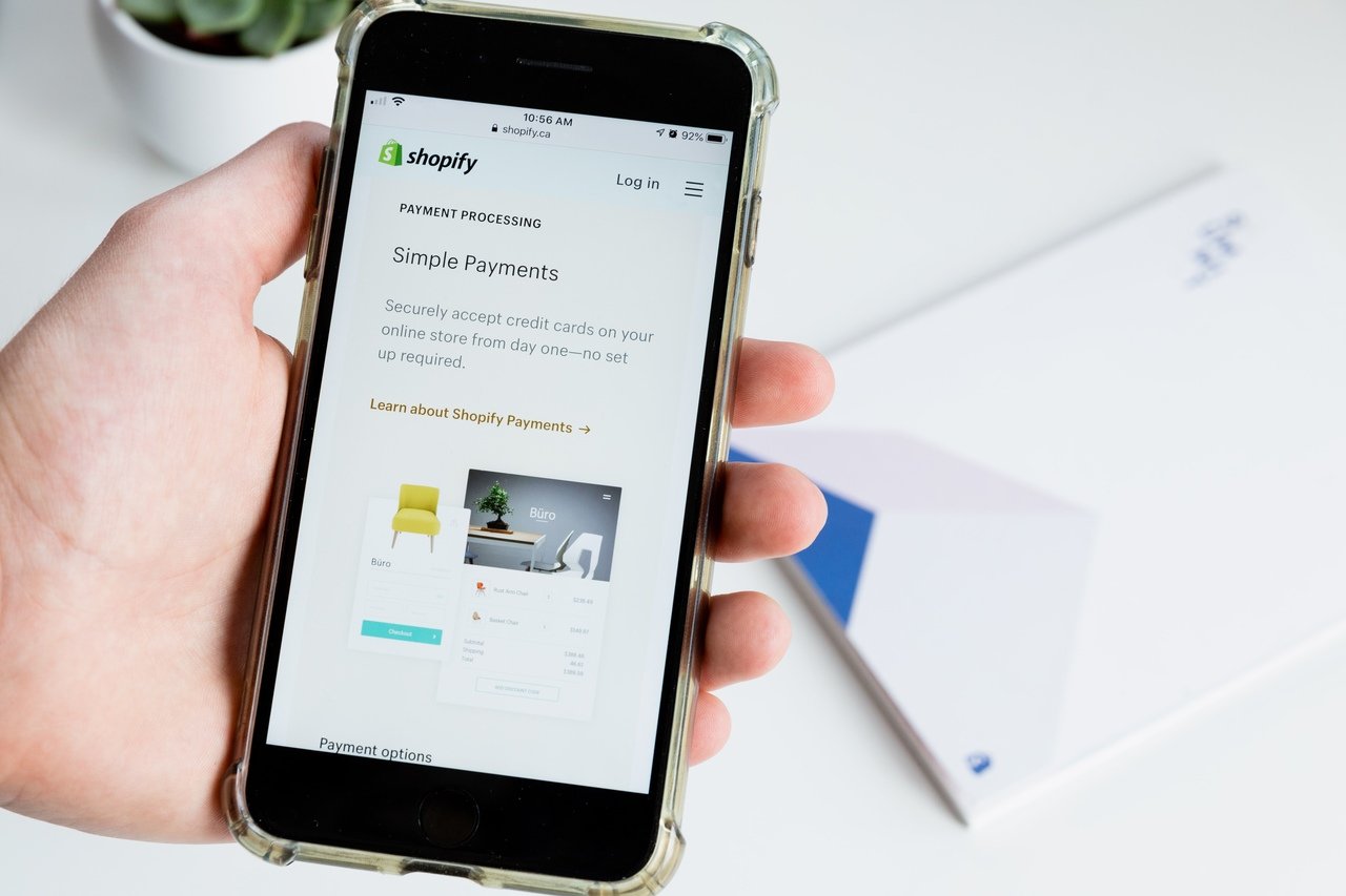 a hand holding a phone that is showing a Shopify store's payment processing page