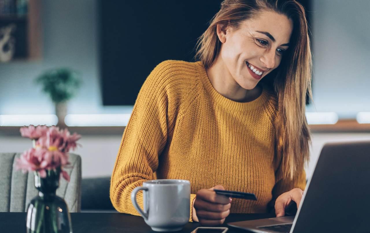 a woman with a long hair and a yellow sweater, as a happy customer, shopping online working with her laptop