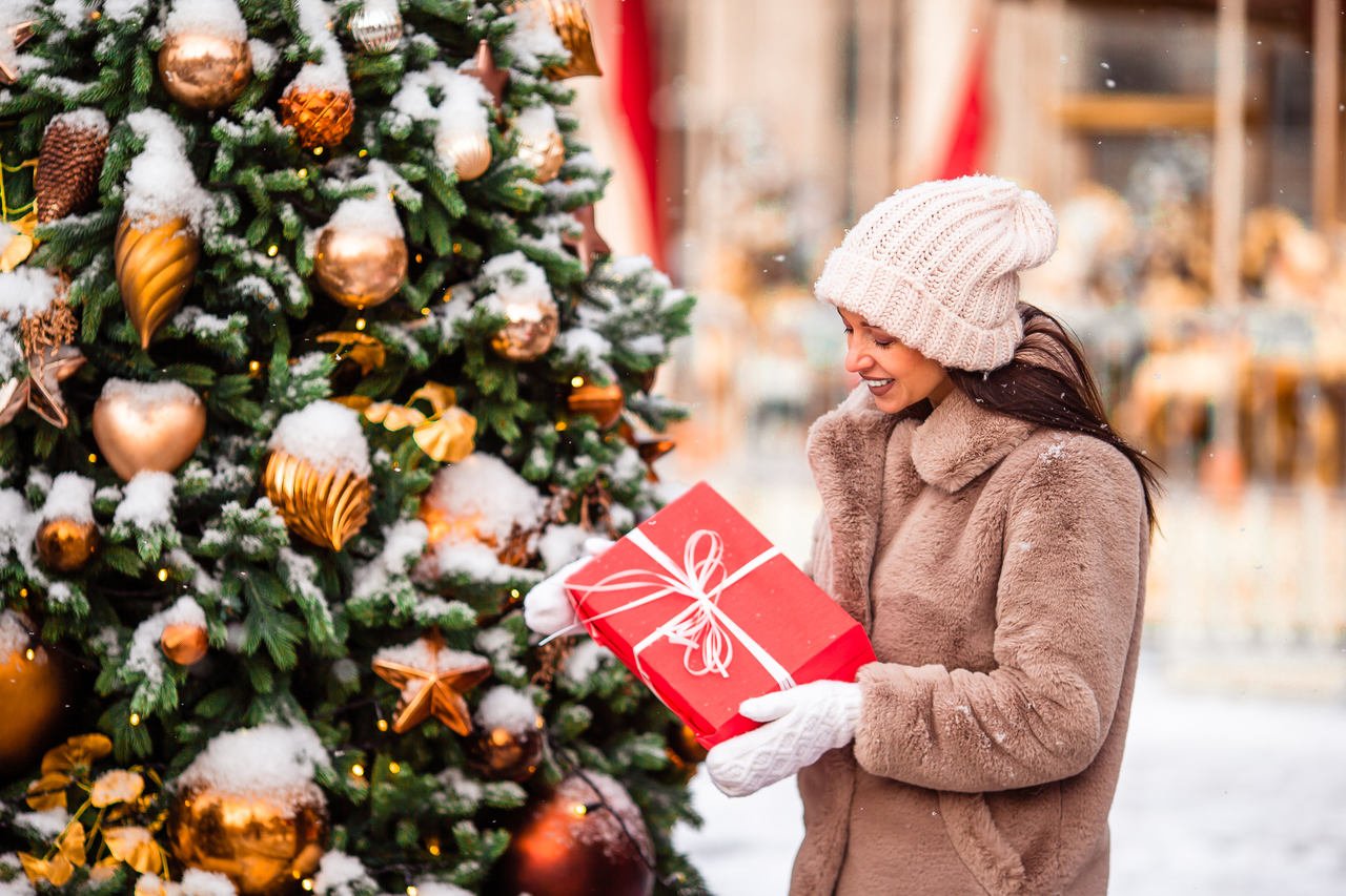 a woman putting a charity gift under tree smiling and wearing gloves and a hat