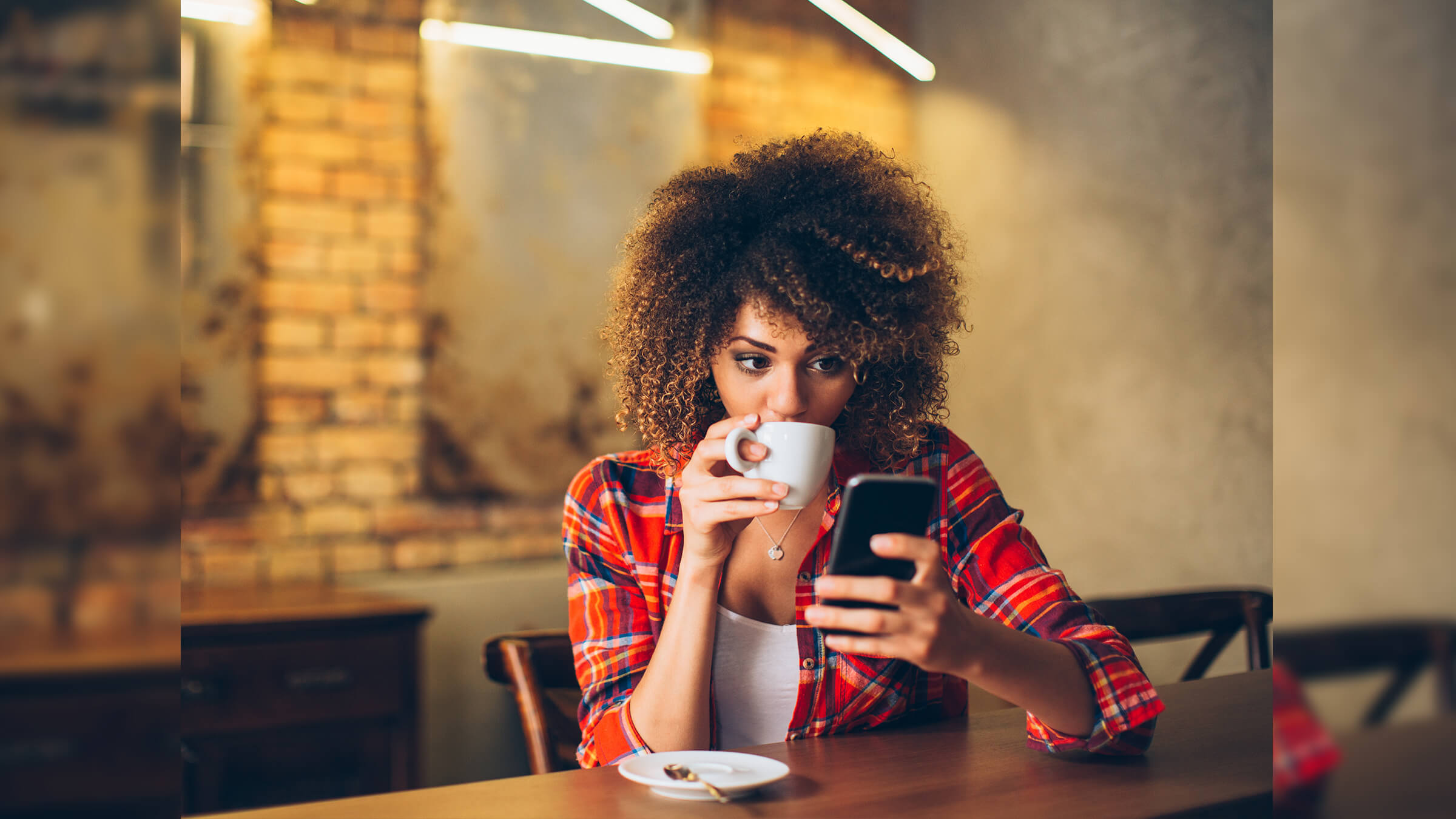 Young woman at cafe drinking coffee and using mobile phone